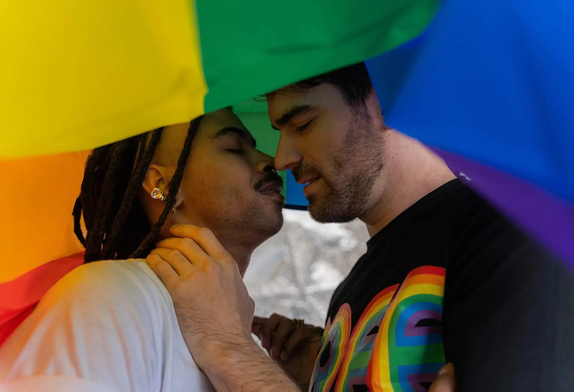 A gay couple poised to kiss under the pride flag.