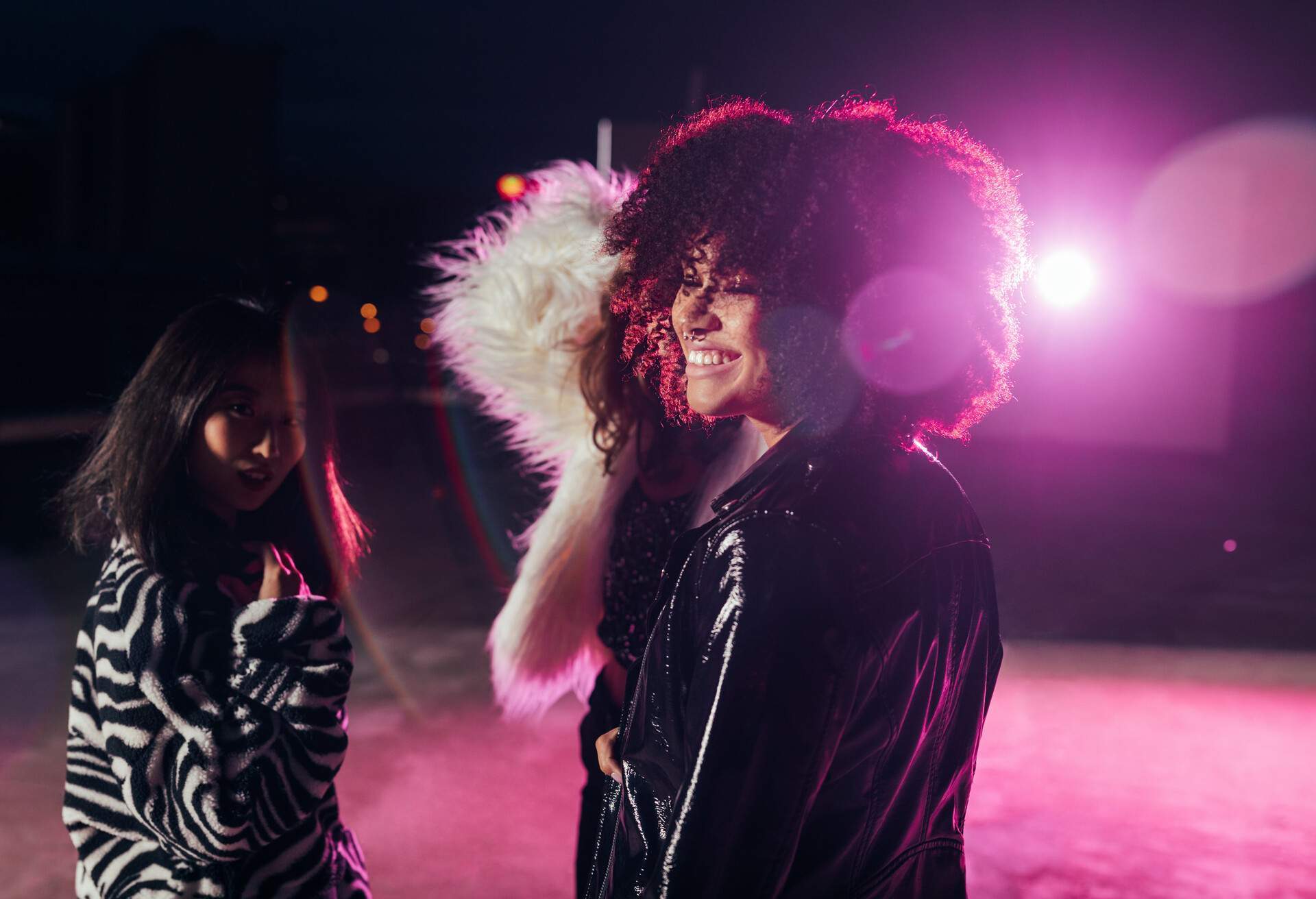 Portrait of two women. One is wearing her faux zebra printed winter jacket and the other is wearing a black leather jacket with purple LED lights on the back.