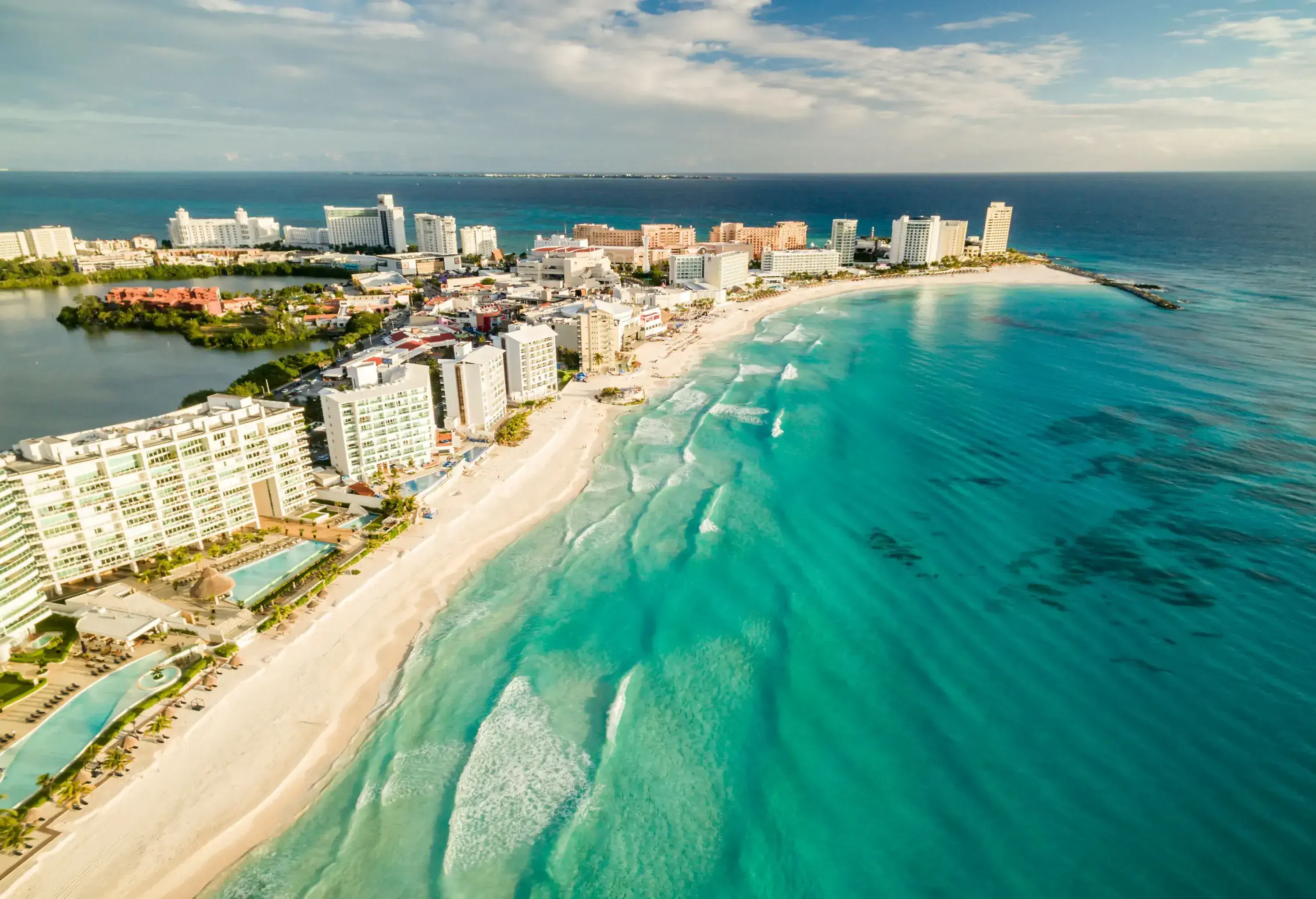 Charming buildings line the pristine beachside, their facades complementing the soft, white sand, while rhythmic waves gently lap against the shore.