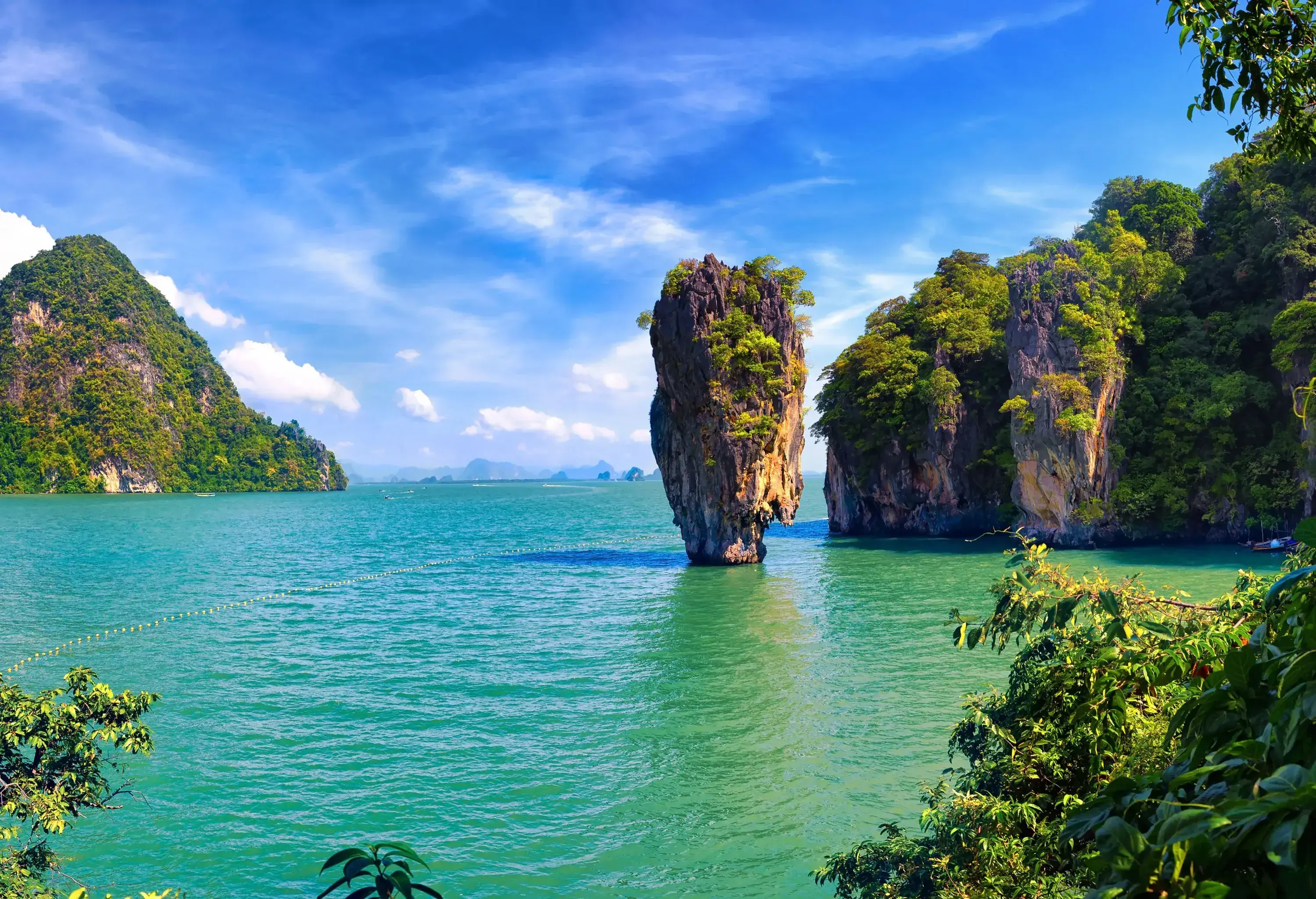 Steep limestone karst towers in the sea under a blue sky with wispy clouds.